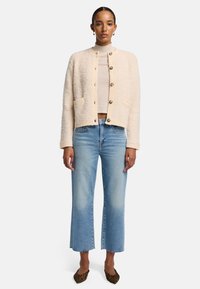 Beige texturerad kofta med rund halsringning, framknäppning och sidofickor, tillsammans med ljusblå utställda jeans och skor med leopardtryck.