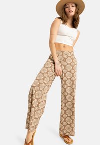 Pantaloni largi dintr-un material maro cu un model floral. Completați cu un top alb strâmt și o pălărie din paie.