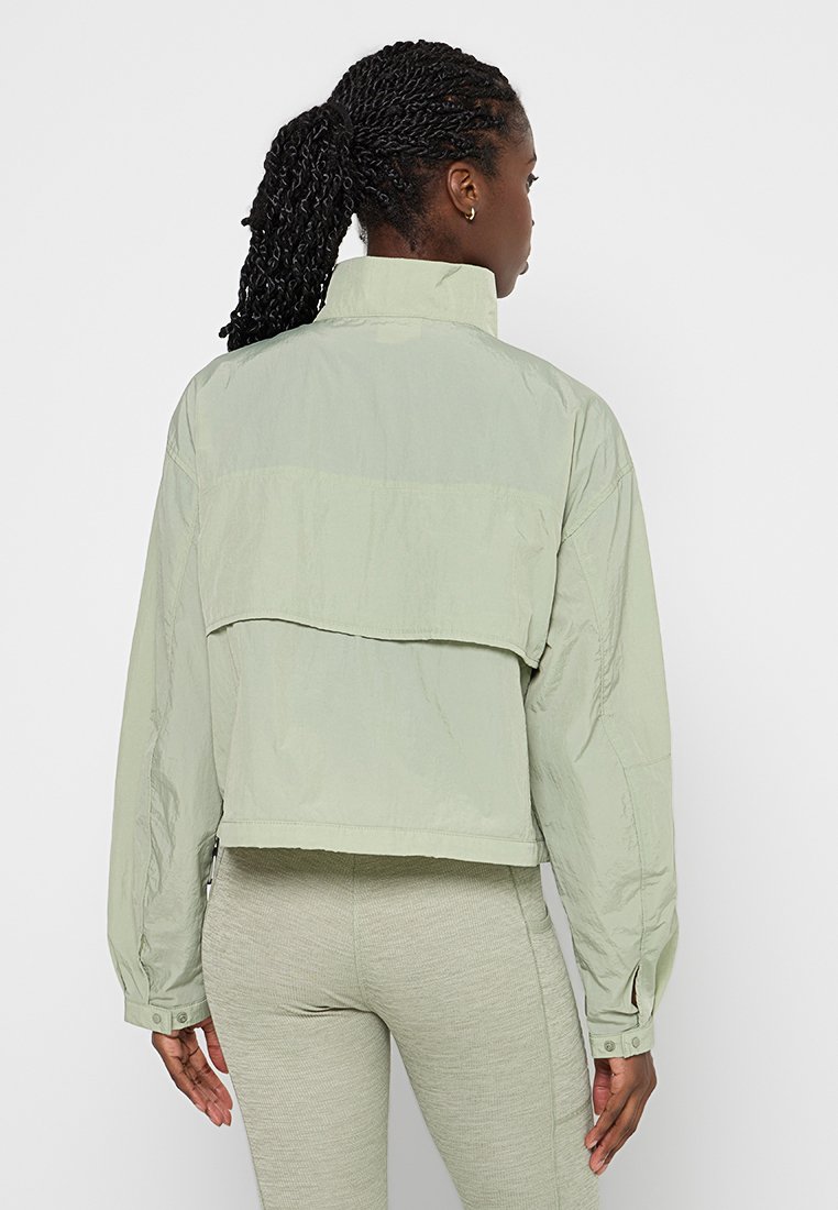 Veste courte vert clair avec un col haut et des manches longues ; présente une texture lisse et légèrement brillante ainsi que des fermetures à boutons sur le côté.