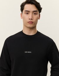 Svart hettegenser med rund hals, lange ermer og hvit brodert tekst "LES DEUX" på brystet. Glatt bomullsmateriale.