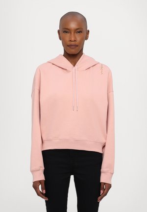 Roosa kapuutsi-hoodie, millel on lühendatud disain, kinnitusnöör ja ribavarrukad. Märkimisväärne kuldne aktsent õlal. Kanda mustade pükstega.
