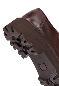 Scarpa in pelle marrone con una suola in gomma spessa e testurizzata, dotata di profondi intagli per una migliore aderenza. Parte superiore liscia con dettagli di cucitura sottili.