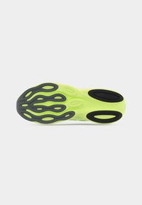 Σόλα αθλητικού παπουτσιού σε νέον πράσινο χρώμα με μαύρα μοτίβα πρόσφυσης, παρουσιάζεται πάνω σε λευκό φόντο.