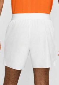 Pantaloni sportivi bianchi con cintura elastica, texture liscia e taglio dritto, progettati per il comfort durante l'attività fisica.