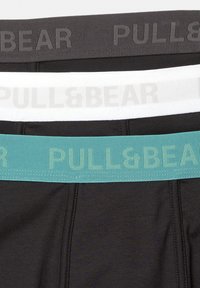 Schwarz-weiße Boxershorts mit türkisfarbenen elastischen Taillenbändern. Jedes Band trägt ein "PULL&BEAR"-Logo in passenden Farben. Glatte Textur.