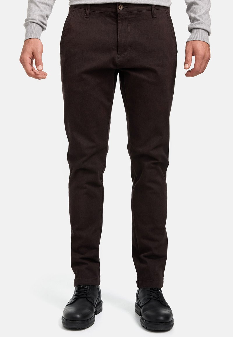 Chinos de color marrón oscuro con un diseño ajustado, que cuentan con un cierre de botón y trabillas para el cinturón. La tela tiene una textura suave, combinada con zapatos negros.