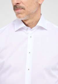 Witte overhemden met een klassieke kraag, voorzien van parelmoeren knopen en een glad, gestructureerd fabric. Tot de derde knop geknoopt.