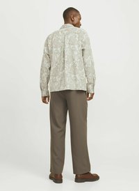Cămașă de culoare deschisă cu un model paisley, asortată cu pantaloni întunecați, lejere și pantofi maro. Cămașa are mâneci lungi și guler.