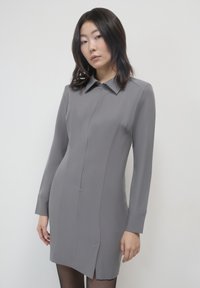 Abito grigio a maniche lunghe con colletto, zip frontale e spacchi laterali. Realizzato in tessuto liscio con una silhouette aderente.