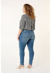 Zwart-wit gestreepte blouse met opgerolde mouwen, gecombineerd met lichtblauwe skinny jeans en beige hoge hakken, gezien van achteren.