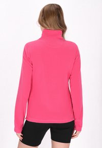 Pullover in pile rosa con colletto alto e maniche lunghe. Texture morbida, design semplice e vestibilità rilassata. Include un orlo liscio in vita.
