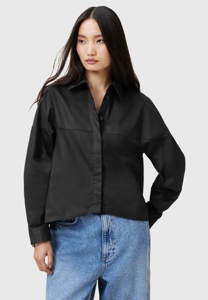 Schwarze Button-up-Hemd mit einem offenen Kragen, langen Ärmeln und lockerer Passform, aus einem glatten Material gefertigt. Kombiniert mit hellblauen Jeans.