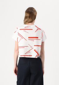 Trumpas baltas marškinėliai su raudonu tekstu ir dryžuotu raštu, kuriuose yra spaudos "KARL" ir "JEANS". Trumpomis rankovėmis, laisvo kirpimo.