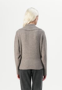 Beżowy sweter z dzianiny z wysokim prążkowanym kołnierzem, luźnym krojem i prążkowanym wykończeniem. Miękka tekstura z delikatnym melanżowym wzorem.