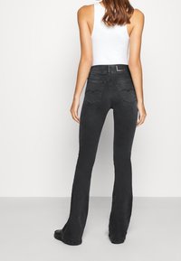 Svart utsvängda jeans med midjehöjd, subtila stygn och två bakfickor. Tillverkade av denimit med en mjuk textur.
