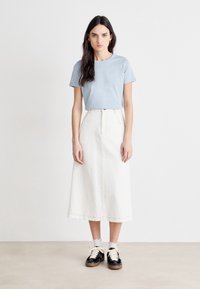 Light blue t-shirt, white denim skirt, black sneakers with cream laces, and logo detail on the shirt. Simple, casual outfit.
