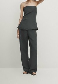 Top sans bretelles gris foncé avec un ourlet peplum, associé à un pantalon large en tissu léger, présenté avec des chaussures noires.