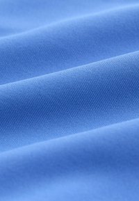 Modrá bavlnená tkanina s hladkou textúrou, zdobená diagonálnymi líniami a jemným leskom, poskladaná do mäkkých, plynulých vĺn.