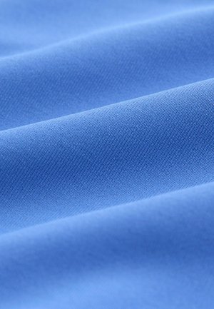 Modrá bavlněná látka s hladkým povrchem, se šikmými pruhy a jemným leskem, složená do měkkých, volně tekoucích vln.