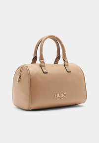 Beige kabelka z umělé kůže zaobleného tvaru, s dvojitými ušima, zlatým logem a zlatými cvočky. Obsahuje zipové uzavření.