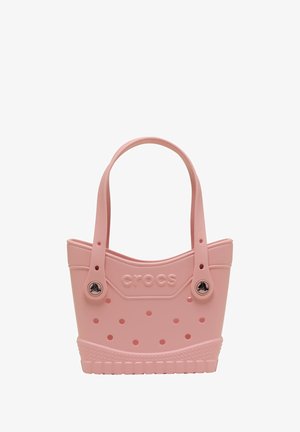 Sac fourre-tout en plastique rose avec un haut arrondi, deux poignées, un corps perforé et une base texturée. Présente le logo "CROCS" et des accents circulaires.