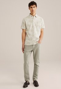 Camisa de botones con una base de color crema claro, con dibujos a línea de flores en marrón. Combinada con pantalones verdes claros y mocasines negros.