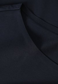 Tissu en coton bleu marine avec une texture lisse. Présente un col arrondi et des coutures fines le long des bords, soulignant une finition nette.