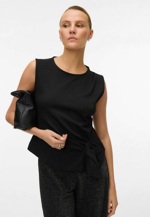 Haut sans manches noir avec un col rond, détail torsadé sur le côté, associé à un pantalon sombre brillant et un sac à main noir texturé.