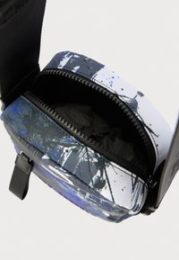 Στρογγυλή τσάντα με φερμουάρ, κατασκευασμένη από πολύχρωμο ύφασμα με μπλε και μαύρα σπιρτούνια. Το εσωτερικό είναι επενδεδυμένο με σκουρόχρωμο ύφασμα.