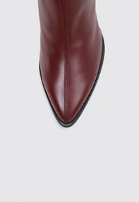 Botín de cuero burdeos con punta afilada, diseño elegante, suela negra y detalle de costura vertical en la parte delantera.