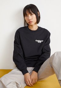 Melna garā piedurkņu džemperis ar "Carhartt WIP" logotipu baltā krāsā uz krūts. Brīvs piegriezums ar ribotām piedurknēm. Strukturēta auduma.