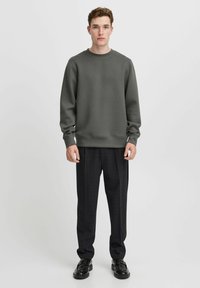 Grauer Sweatshirt mit Rundhalsausschnitt, gerippten Bündchen, getragen mit dunklen Karo-Hosen und schwarzen Schuhen. Glattes Material mit einfachem Design.