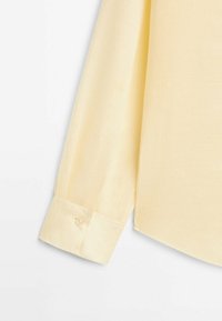 Chemise jaune à manches longues avec un poignet boutonné, tissu en coton lisse, coupe décontractée, avec un léger éclat et des coutures soignées.