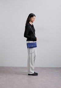 Blue leather crossbody bag with a silver chain strap, sleek design, and logo detail, worn with gray sweatpants and a black ribbed top.
