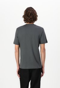 Grå kortermet t-skjorte med rund hals, laget av myk bomullsstoff, med enkel design og avslappet passform. Bakfra vises.