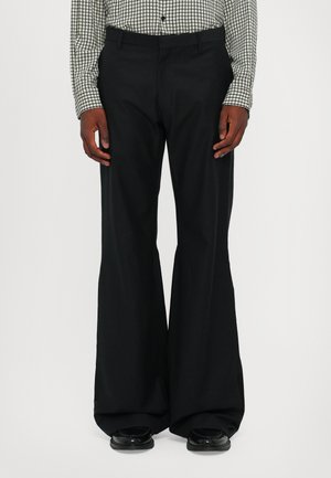 Schwarze, weit geschnittene Hosen mit glatter Textur, ausgestattet mit einer maßgeschneiderten Taille und einer fließenden Silhouette, kombiniert mit schwarzen Schuhen.
