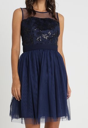 Marineblå kjole med en tætsiddende krop med blomsterbroderi og palietter, gennemsigtig halsudskæring og en flydende tylskørt.