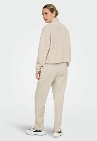 Beige fleece pullover with a high collar, cropped design, and elasticated cuffs, paired with matching tapered pants and chunky sneakers.