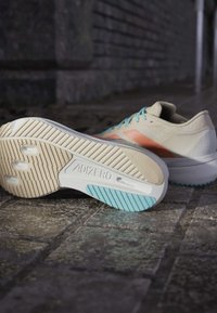 Light-colored Adidas Adizero running shoes with blue laces resting on a stone pavement, one shoe showing the sole.