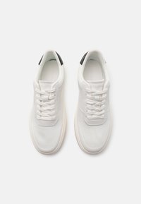 Sneakers bianchi con tomaia in rete, punta rotonda, chiusura con lacci e un accento nero sul tallone. Suola morbida e flessibile per il massimo comfort.