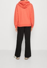 Coral oversized hoodie with a hood and ribbed cuffs, paired with black wide-leg pants. The outfit features a relaxed fit and soft texture.