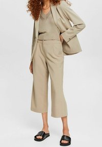 Blazer beige a medida sobre una blusa de punto a juego, combinado con pantalones anchos de pierna corta y sandalias de cuero negras. Tejido suave y textura sutil.