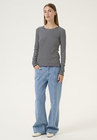 Camicia a maniche lunghe a righe in bianco e nero, abbinata a pantaloni larghi blu chiaro con linee di texture verticali, indossata con scarpe bianche.