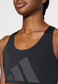 Μαύρο αθλητικό crop top από υφή δροσερού, αεριζόμενου υφάσματος με λαιμόκοψη scoop και αντανακλαστικό σχέδιο λογότυπου στο μπροστινό μέρος.