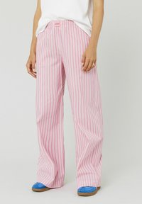 Pantalons larges rose clair avec des rayures verticales blanches, dotés d'une ceinture élastique. Le tissu est doux et offre une coupe décontractée.