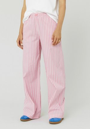 Pantalons larges rose clair avec des rayures verticales blanches, dotés d'une ceinture élastique. Le tissu est doux et offre une coupe décontractée.