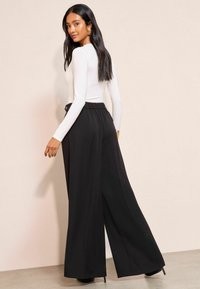 Černé kalhoty s širokými nohavicemi, vysokým pasem a sklady, v kombinaci s přiléhavým bílým topem s dlouhým rukávem. Hladká látka a elegantní silueta.