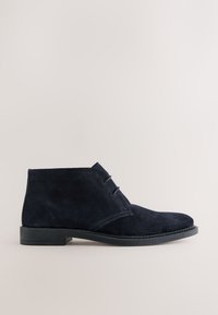 Marineblaue Wildleder-Stiefeletten mit glatter Textur, vorne mit zwei Schnürsenkeln, abgerundeter Zehenpartie und flacher Gummisohle.