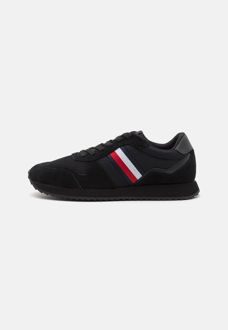 Sneaker nera con tomaia in rete e suede, caratterizzata da strisce laterali rosse, bianche e blu. Suola testurizzata con un design a profilo basso.
