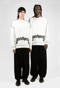 Sweatshirts surdimensionnés blancs avec le texte noir "pastedpur", pantalons larges noirs et chaussures noires. Tissu lisse, coupe décontractée.